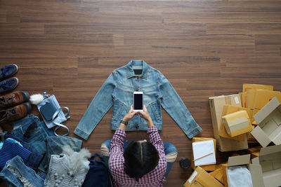 Directly above shot of businesswoman photographing denim shirt while sitting on wooden floor