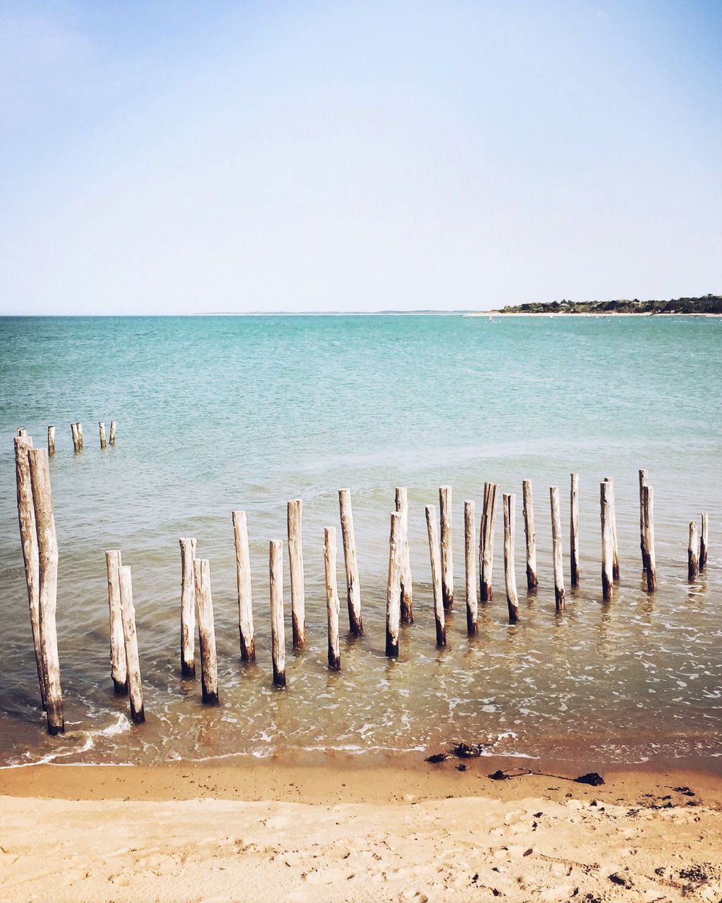 sea, water, horizon over water, beach, tranquil scene, tranquility, shore, scenics, beauty in nature, blue, nature, wooden post, idyllic, sky, calm, day, remote, outdoors, no people, non-urban scene, ocean, coastline