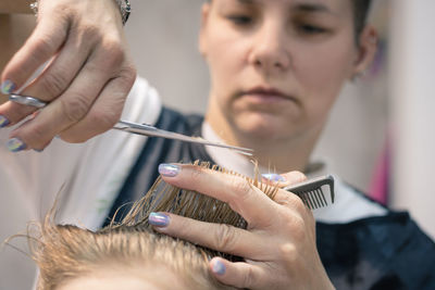 Close-up of barber cutting boy hair in salon