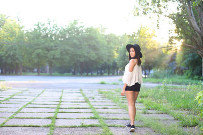 Full length portrait of young woman standing against trees