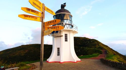 Low angle view of road signs by lighthouse on cliff against sky