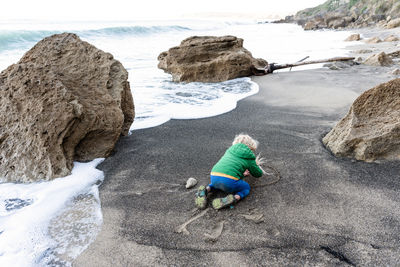 Small child writing in sand on beach in new zealand