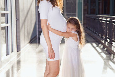 Mother and daughter standing against wall