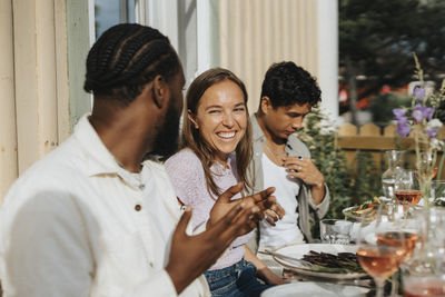 Happy young woman looking at male friend talking during dinner party at cafe