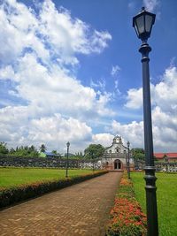 Street light on footpath against cloudy sky