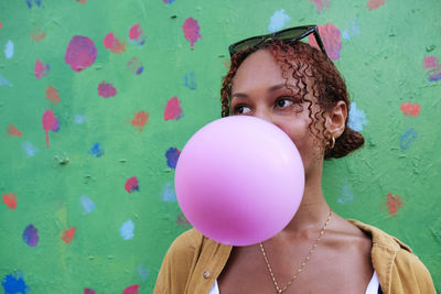 Young woman blowing bubble gum in front of wall