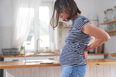 A young pregnant woman holds her back with her hands.  the concept of back pain during pregnancy