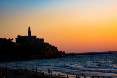 Silhouette buildings by sea against romantic sky at sunset