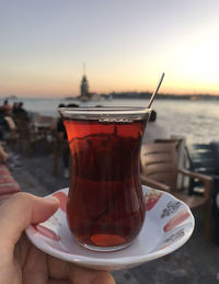 Close-up of hand holding drink against sky during sunset