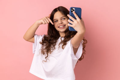 Midsection of woman using mobile phone against pink background