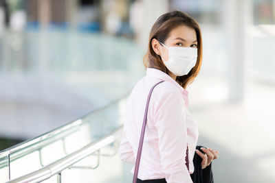 Portrait of businesswoman wearing mask standing by railing outdoors