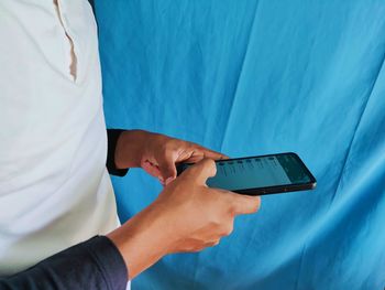 Midsection of man using mobile phone against blue sky