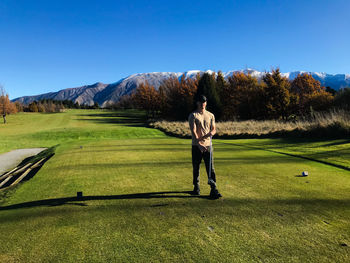 Rear view of man walking on golf course against clear sky