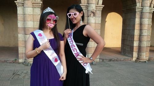 Portrait of smiling females with props while standing against building