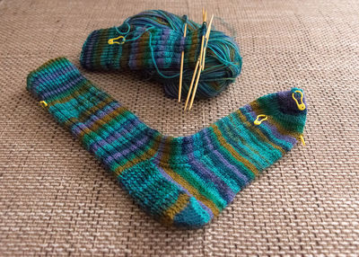 Knitted sock knitted with green striped yarn, wooden knitting needles and a ball of wool yarn