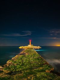 Lighthouse by sea against sky at night