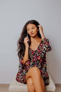 Beautiful young woman sitting against wall