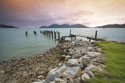 Wooden posts in sea against sky during sunset