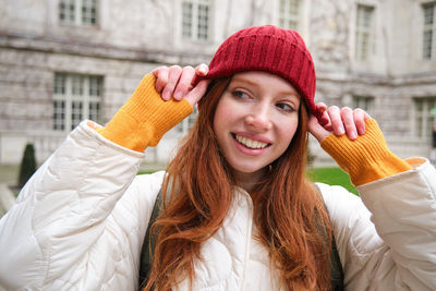 Portrait of young woman standing against buildings in city