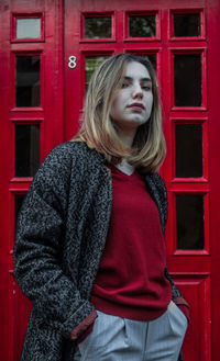 Beautiful young woman standing against red wall