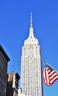 Us flag in front of empire state building. low angle view of buildings against clear blue sky.