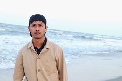 Portrait of young man standing at beach against sky