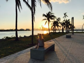 Rear view of woman sitting on beach during sunset