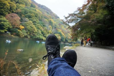 Low section of person wearing black shoes by lake