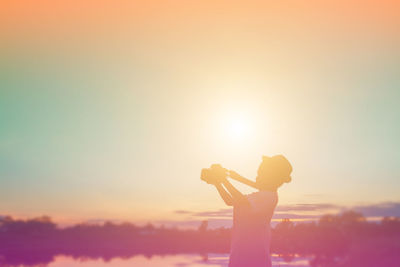 Side view of silhouette woman standing against orange sky