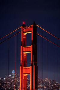 Illuminated suspension bridge in city against sky at night