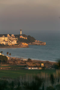 Buildings by sea against sky during sunset