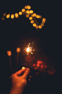 Cropped hand of woman holding sparkler at night