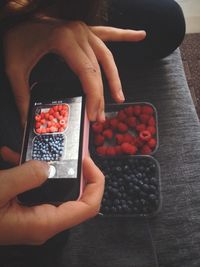 Female photographing raspberry and blueberry with mobile phone