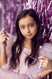 Beautiful girl with big eyes in a pink dress stands against the background of new year's tinsel