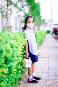 Full length portrait of girl wearing mask standing on footpath