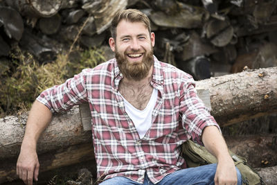 Portrait of laughing bearded man sitting on stack of wood