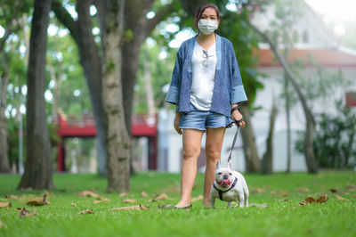Woman in medical mask standing and a white french bulldog with a leash.