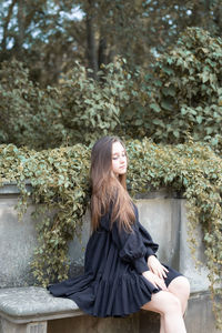 Young woman looking away while sitting on tree