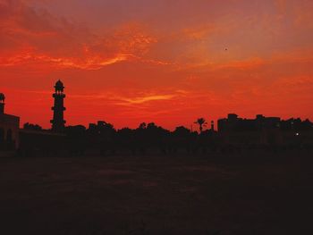 Silhouette buildings on field against orange sky