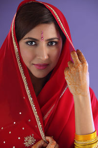 Portrait of beautiful indian woman in red sari against purple background