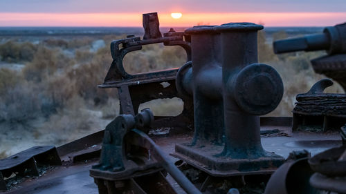 Close-up of rusty metal by sea against sky during sunset