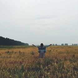 Rear view of woman with arms outstretched standing on grassy field