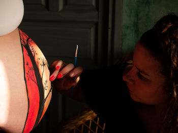 Woman painting on pregnant friend belly