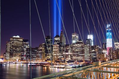 Illuminated bridge over river by buildings against sky at night