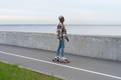 Active urban lifestyle. african girl riding longboard at seaside road. smiling woman on skateboard