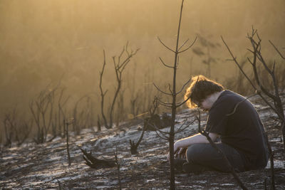 Side view of young man sitting on field during sunset