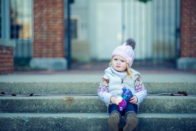 Portrait of cute baby girl in warm clothing sitting on steps