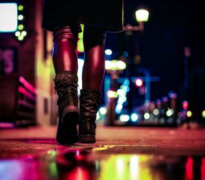 Low section of woman standing on illuminated street