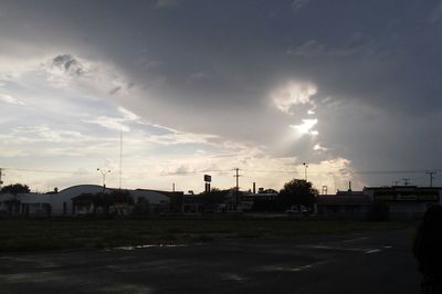 Silhouette buildings by street against sky during sunset