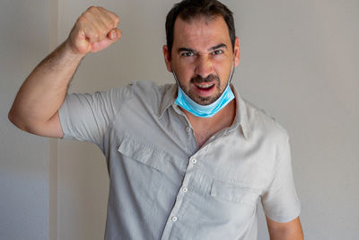 Portrait of man wearing flu mask gesturing while standing against white wall